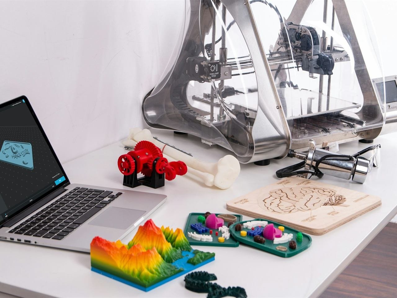 Stampante 3D, computer portatile e oggetti stampati su un tavolo di lavoro